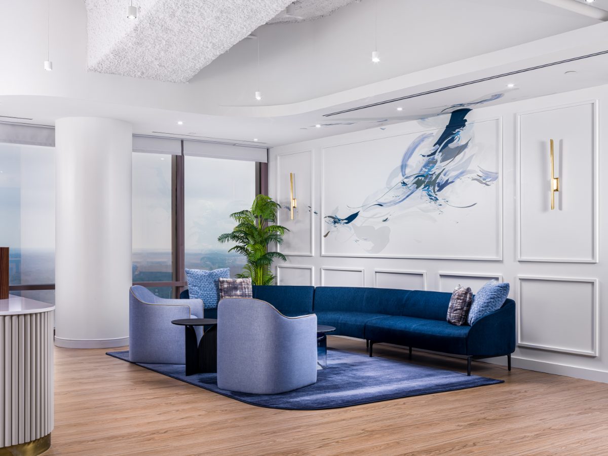 JAMS Atlanta reception lounge at Promenade Tower — navy velvet sectional, light blue chairs, navy rug, white panel wainscoting, abstract blue ink artwork.