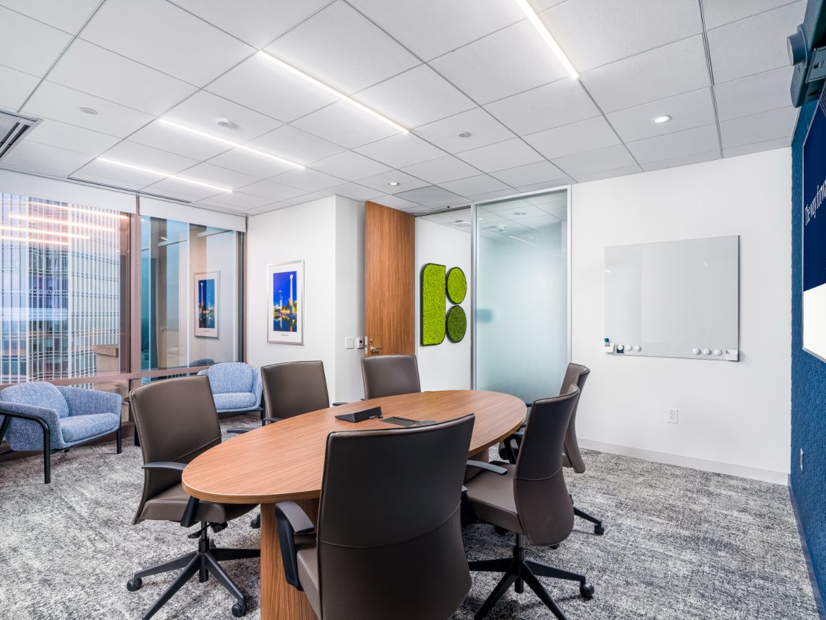 JAMS Atlanta oval conference room at Promenade Tower — walnut oval table, dark leather chairs, blue caucus tub chairs, glass whiteboard, moss-art wall panel.