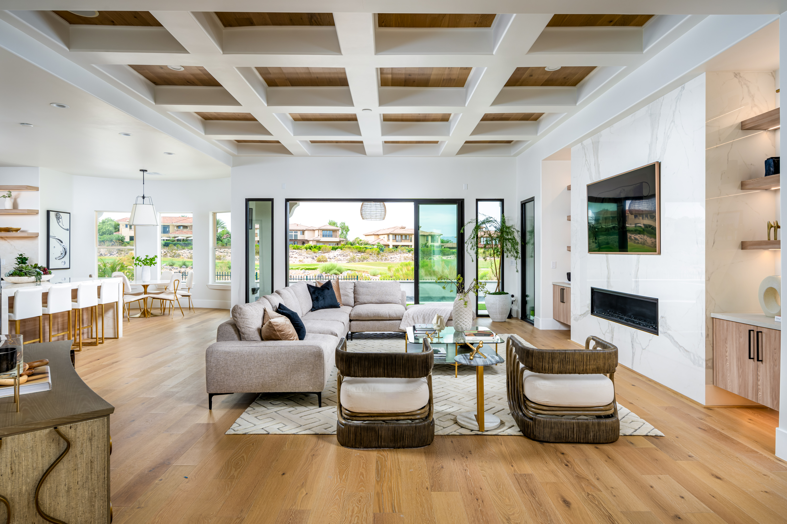 Living Room at a Stately modern transitional luxury home in Las Vegas (1533 TS) — white-and-wood coffered ceiling, marble fireplace, grey sectional, corduroy stools.