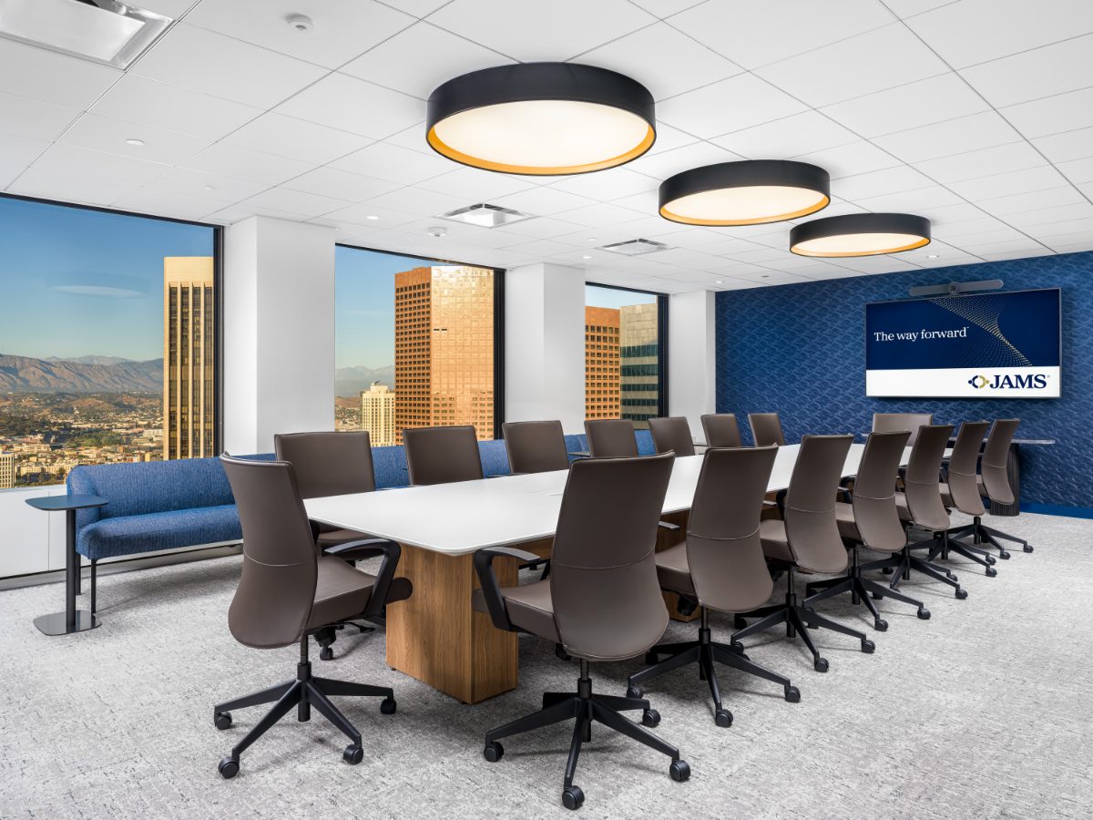 JAMS LA Conference Room 35 from the bench angle — white-quartz table, charcoal leather chairs, drum pendants, periwinkle window bench, sunlit downtown tower view.