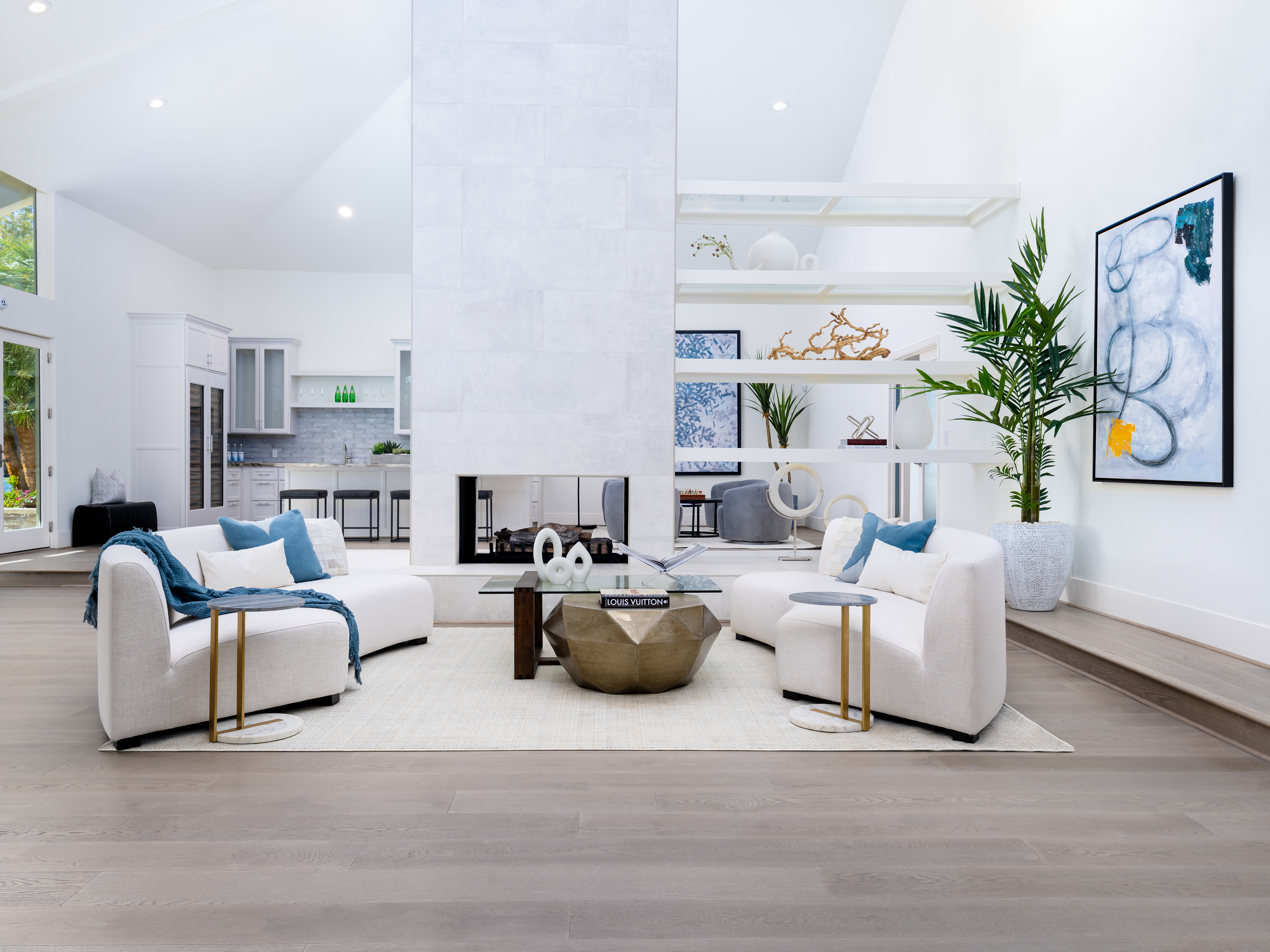 Living Room at a Stately open contemporary home in Las Vegas (2327 AD) — vaulted ceiling, central fireplace, faceted metallic coffee table, blue accent art.