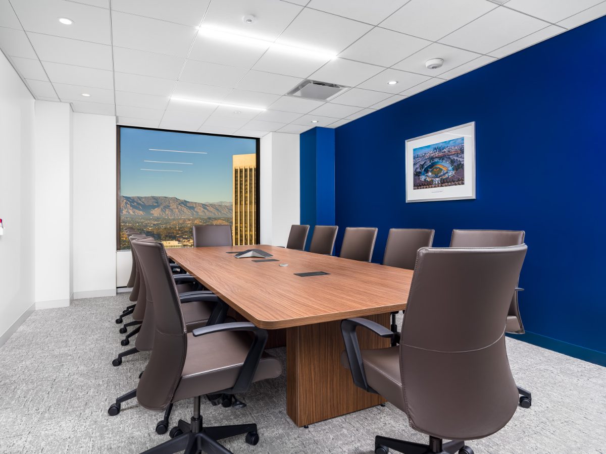 JAMS LA Conference Room 38 — walnut table, brown leather chairs, cobalt feature wall with Dodger Stadium print, San Gabriels through the corner window.