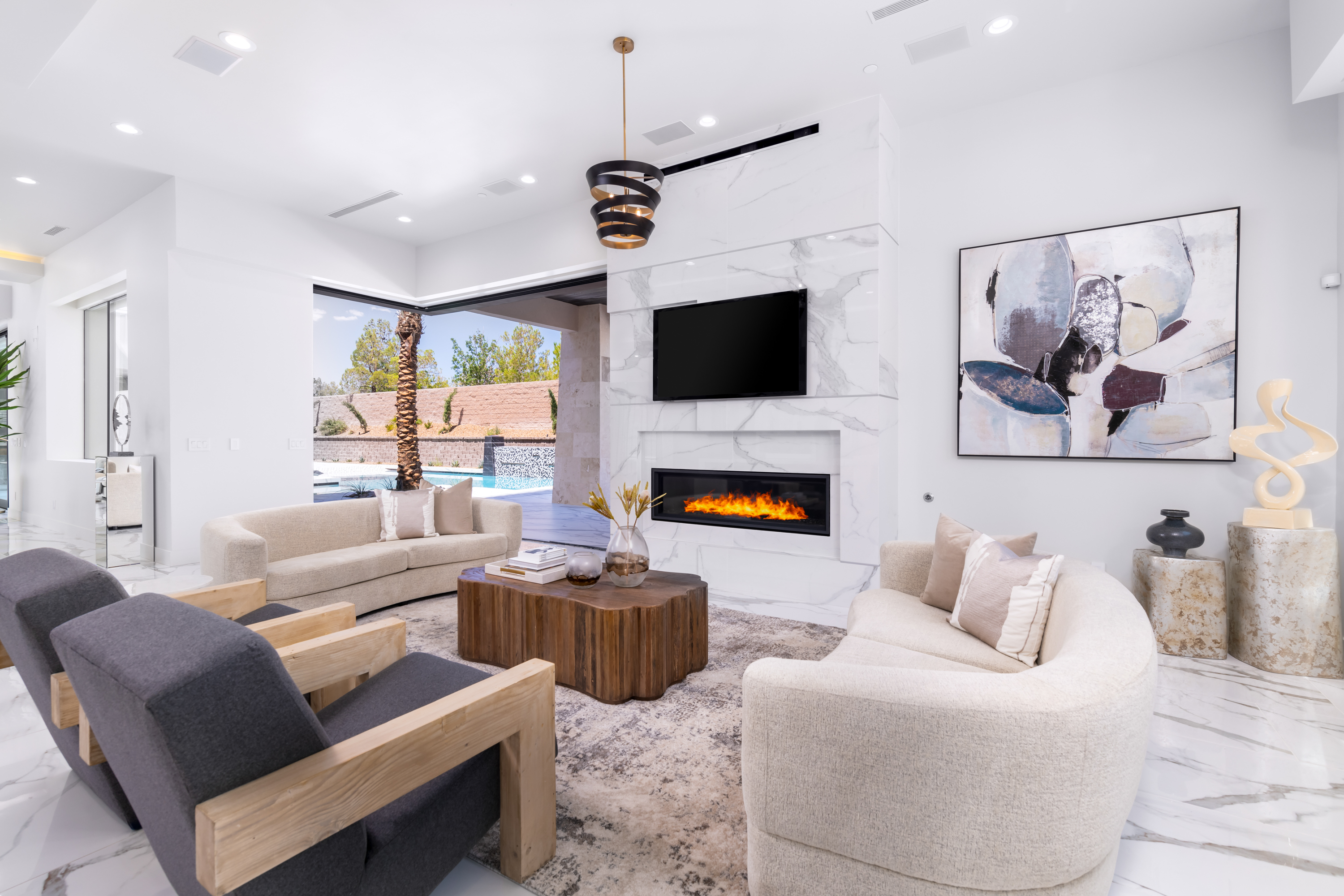 Living Room at a Stately modern desert resort home in Las Vegas (38 RA) — marble fireplace surround, walnut accent stool, abstract art, palm view.