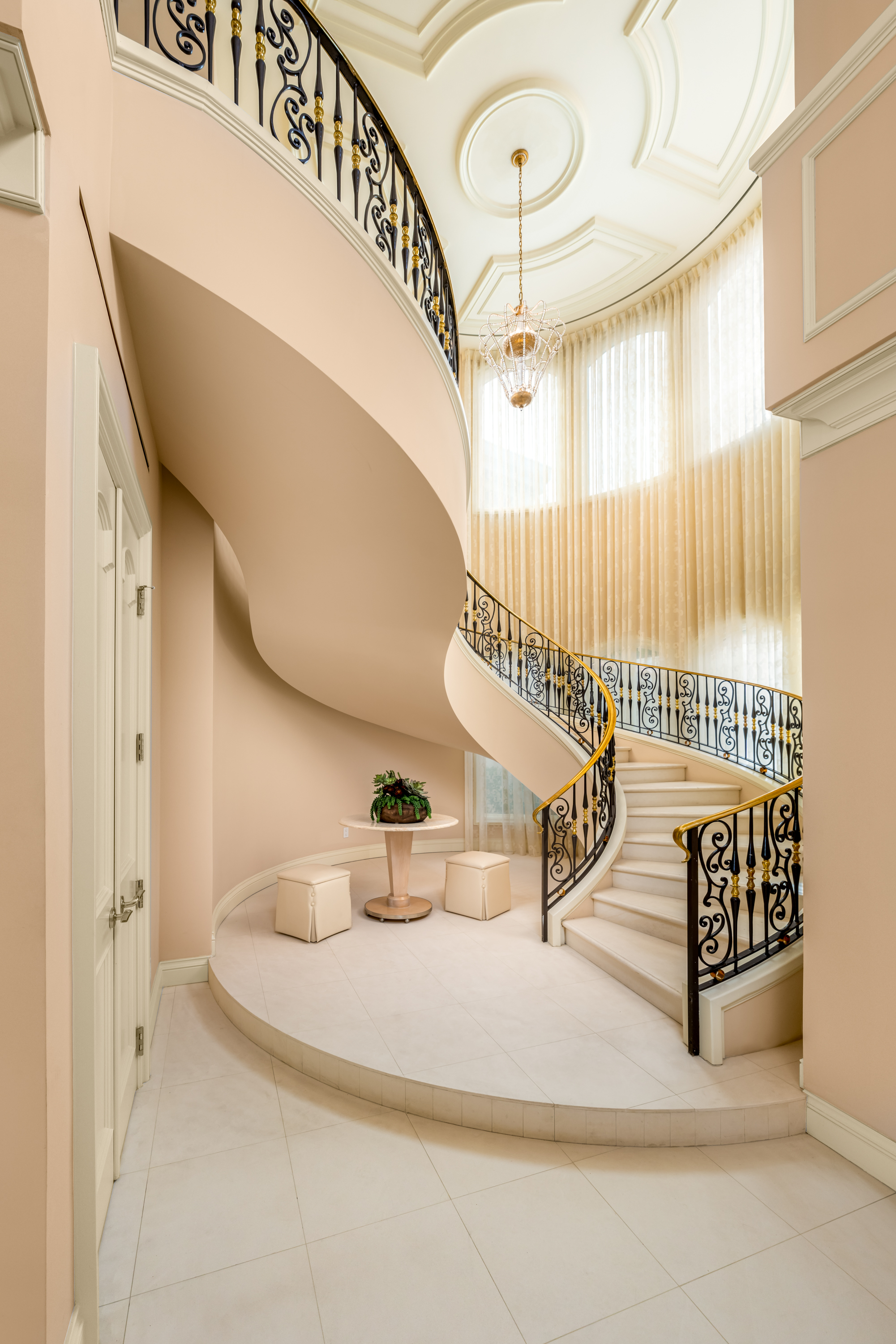 Entrance at a Stately glam estate home in Las Vegas (5114 SHD) — two-story curtains, paired gold-base ottomans, marble fireplace, panoramic view.