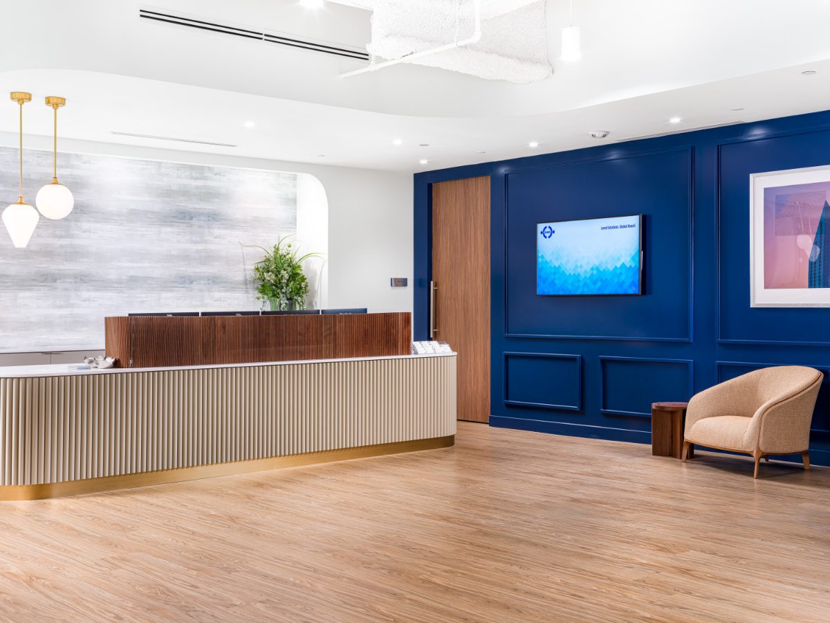 JAMS Dallas front lobby at Sherry Lane Place — fluted reception desk with brass kick plate, navy paneled accent wall, brass pendant globes, blond plank floor.
