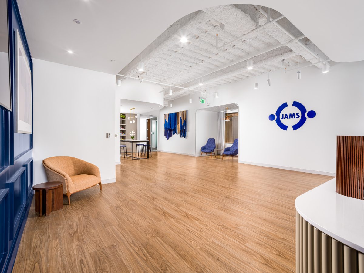 JAMS Dallas reception floor at Sherry Lane Place — blond wood plank floor leading to the JAMS brand logo on a white wall, tan tub chair, blue paneled accent walls.