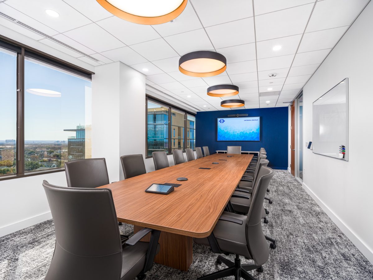 JAMS Dallas large conference room at Sherry Lane Place — walnut table, grey leather chairs, three amber drum pendants, cobalt accent wall with display, balcony view.
