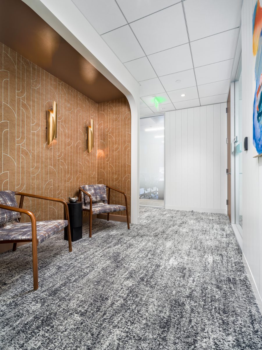 Quiet hallway lounge at JAMS Washington, D.C. — caramel-pattern alcove with brass sconces and two wood-framed plaid chairs in a corridor by the conference rooms.
