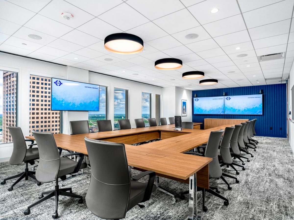 JAMS MN boardroom — U-shape honey table, grey leather chairs, four drum pendants, cobalt board-and-batten wall with twin JAMS displays, downtown Minneapolis view.
