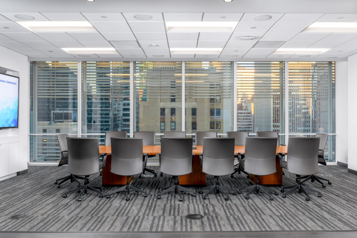 JAMS IAC large boardroom — long cherry table on twin plinths, ~14 grey leather chairs, three walls of louvered windows, JAMS display on left wall.