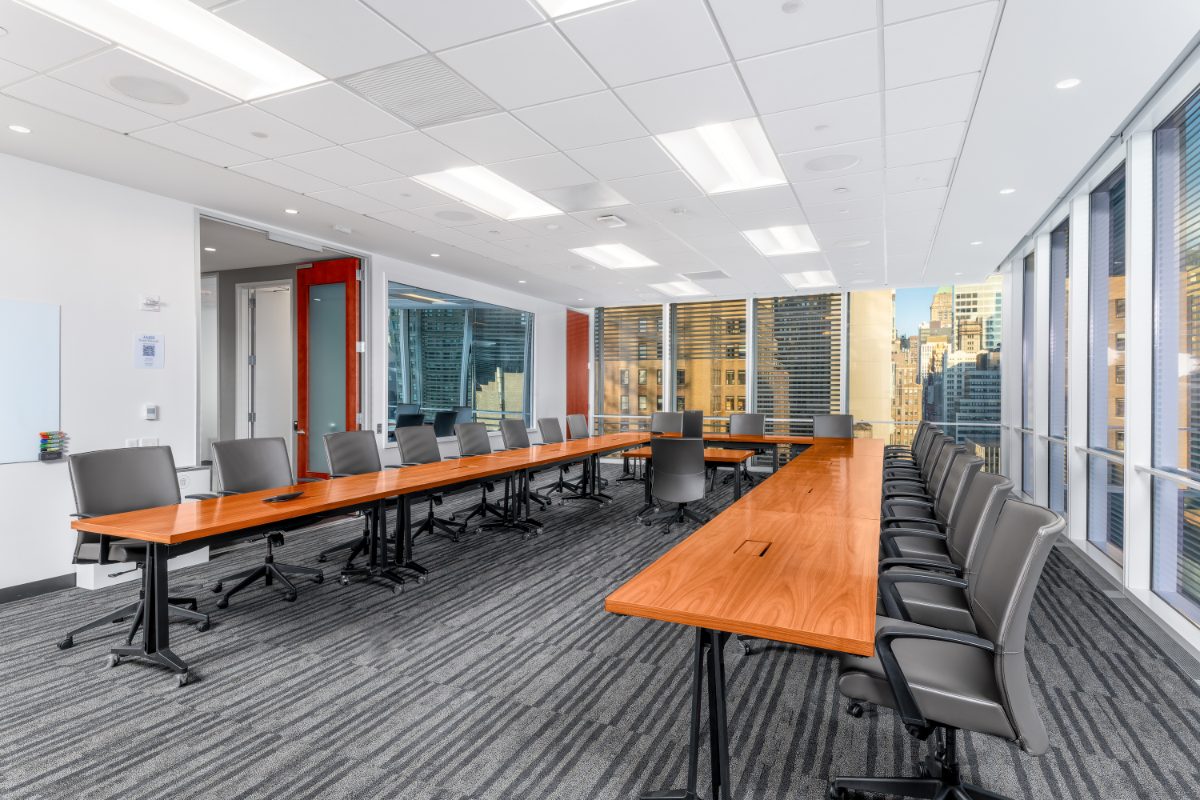 Conference Room 18 at JAMS NY IAC — corner suite, cherry horseshoe for sixteen, mixed mesh and leather chairs, translation-booth window, two walls of skyline.