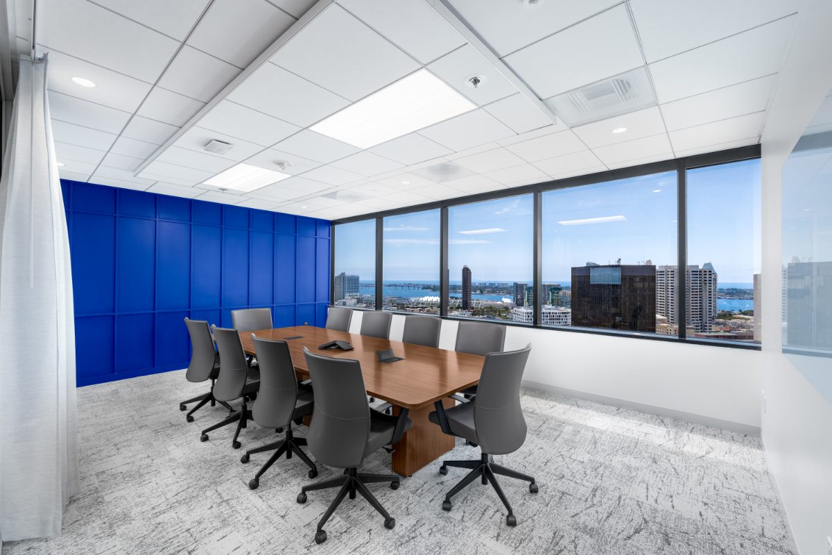 JAMS San Diego mediation room — cherry table with grey leather chairs along windows onto the bay, Convention Center, and Coronado Bridge; cobalt wall opposite.